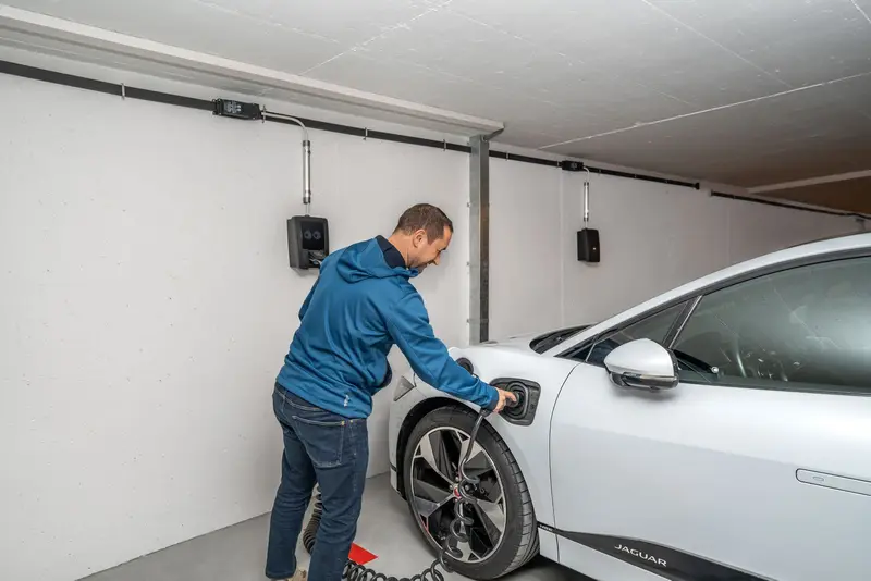 Installateur sluit een elektrische auto aan op een net gemonteerde wandlader in een lichte garage
