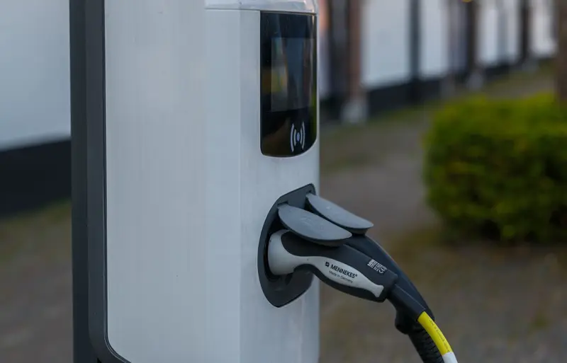 Laadpaal met aangesloten laadkabel in een licht Nederlands woonstraatje